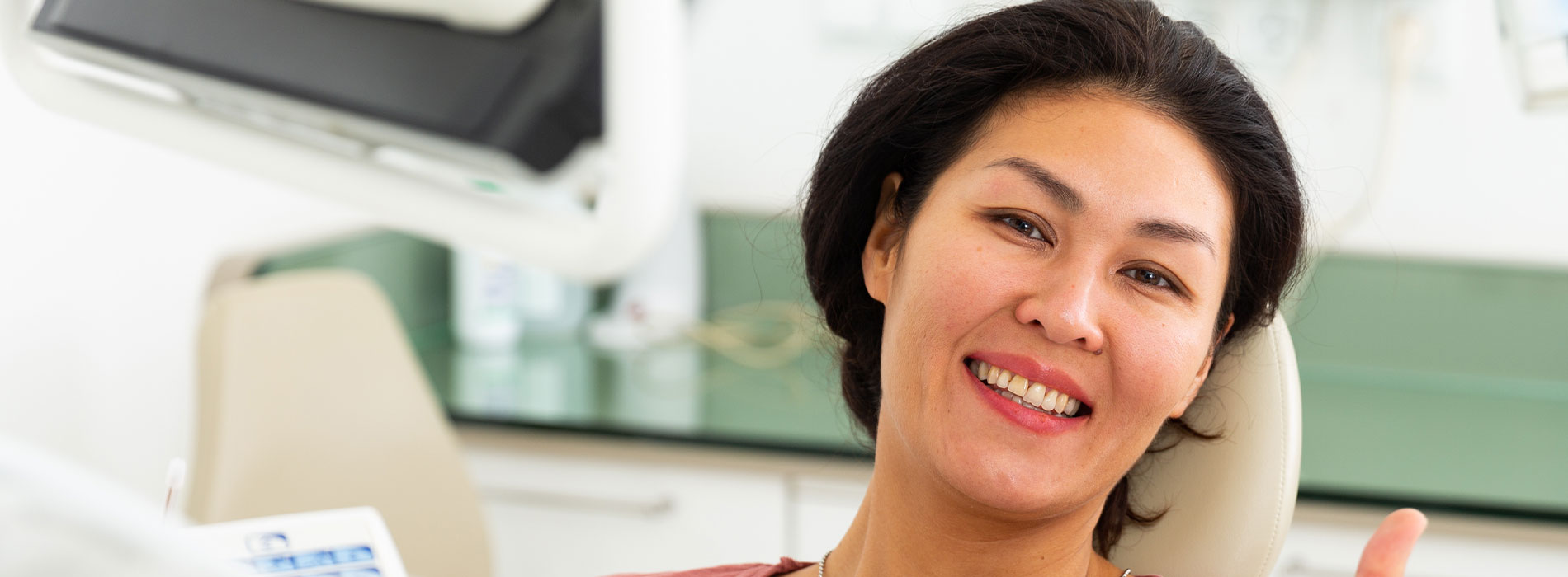 A woman with a big smile, sitting in an orthodontist's chair.