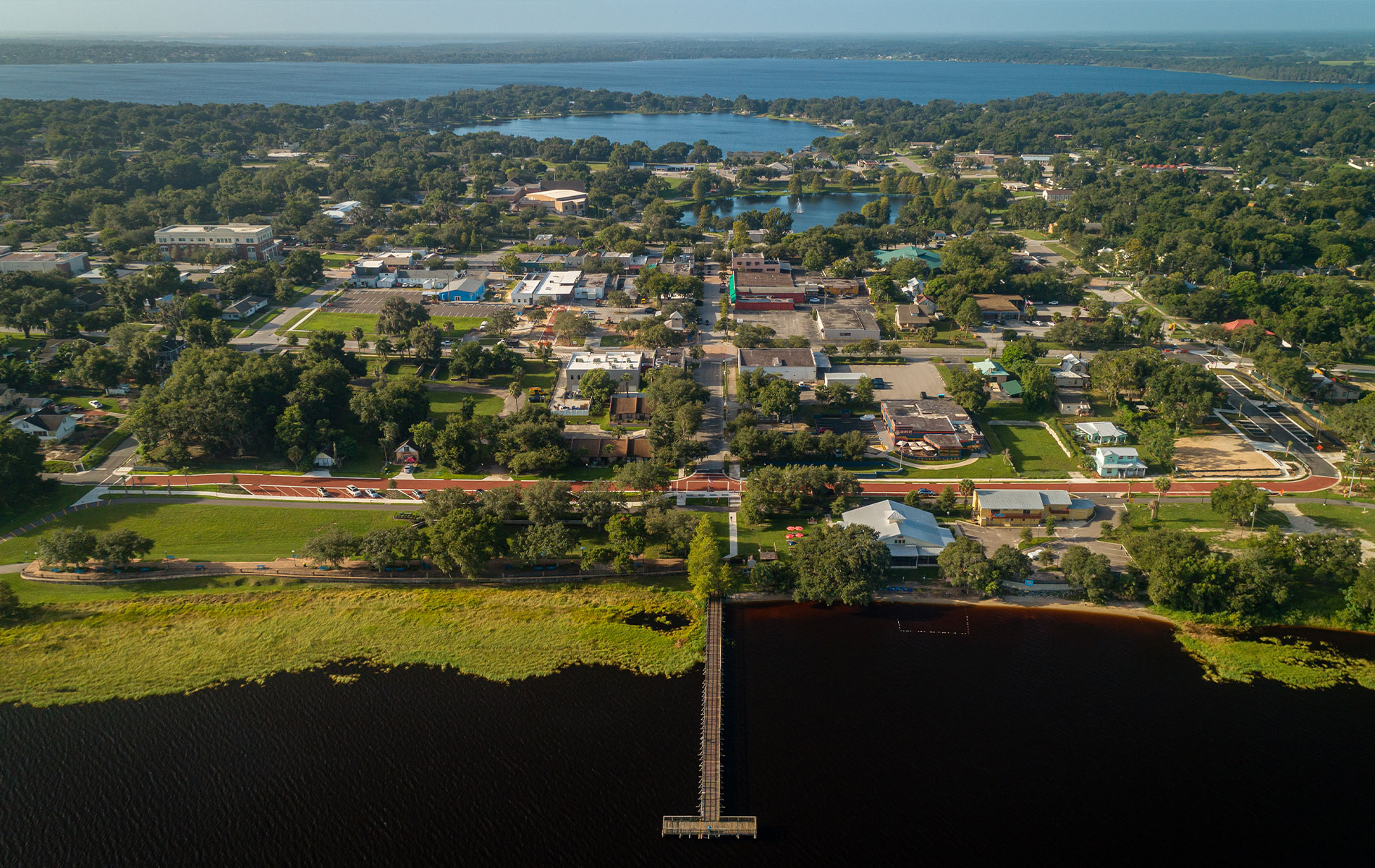 Aerial view of a town with a body of water, surrounded by greenery and buildings.