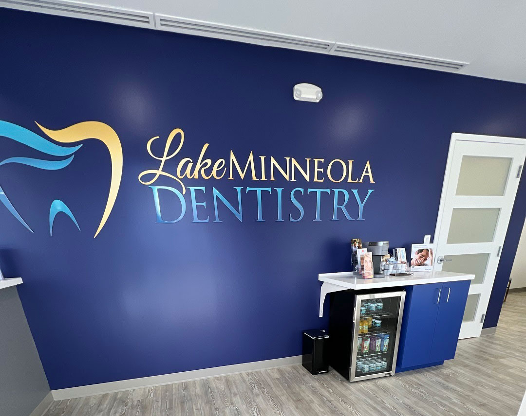 The image is of an interior space with a blue wall featuring a logo and text that reads 'Lake Minneola Dentistry.' Below the logo, there's a sign indicating it's a dental clinic.