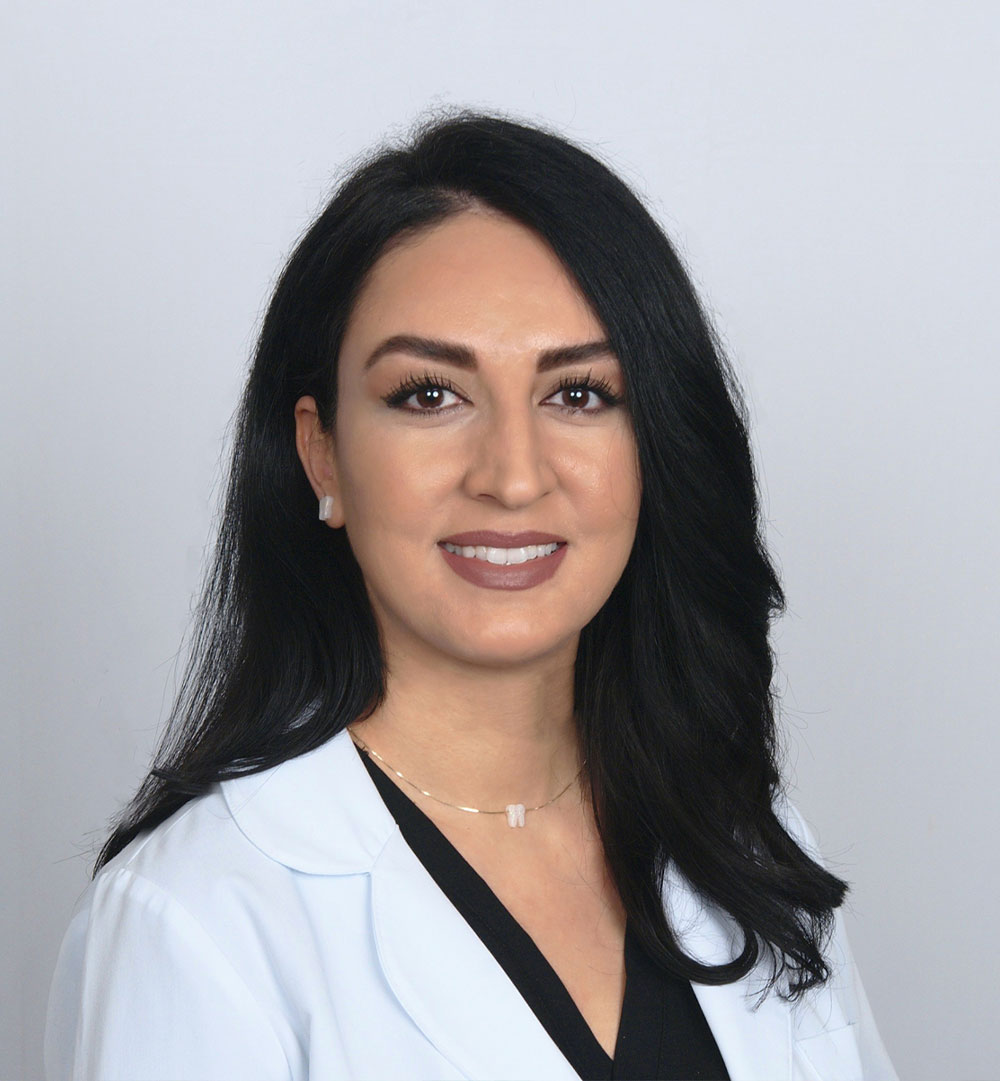 A woman wearing a white lab coat, standing against a white background.
