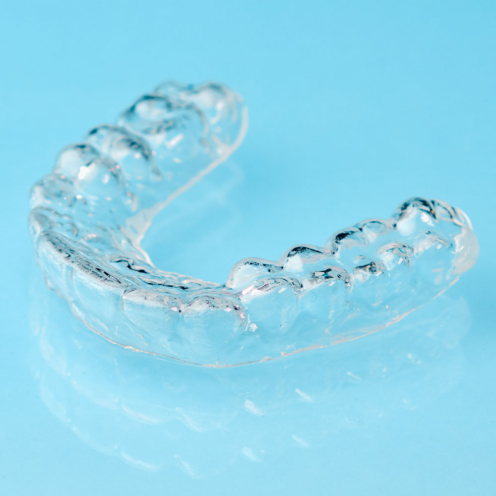 The image shows a clear plastic dental retainer with multiple teeth-shaped indentations, placed on a blue background.