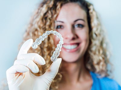 A woman wearing a white glove holds up a clear dental retainer.