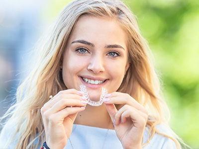 A young woman is smiling, holding a toothbrush with a toothpaste-covered bristle.