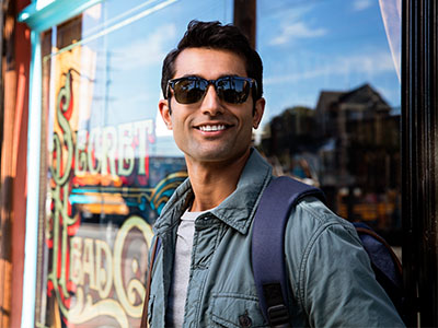 The image features a man standing in front of a storefront window, wearing sunglasses and a backpack.