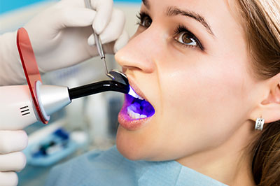 A woman is receiving a dental implant procedure, with a dentist using a specialized device to place the implant.