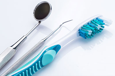 The image features a collection of dental tools, including a toothbrush with blue bristles and a pair of scissors, placed on a white background.