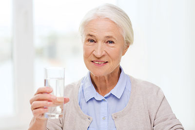 An older woman is holding a glass of water to her mouth.