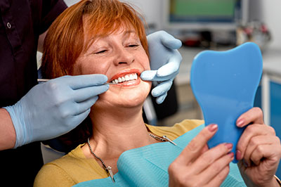 A woman in a dental chair receiving a teeth cleaning with a smiling hygienist.