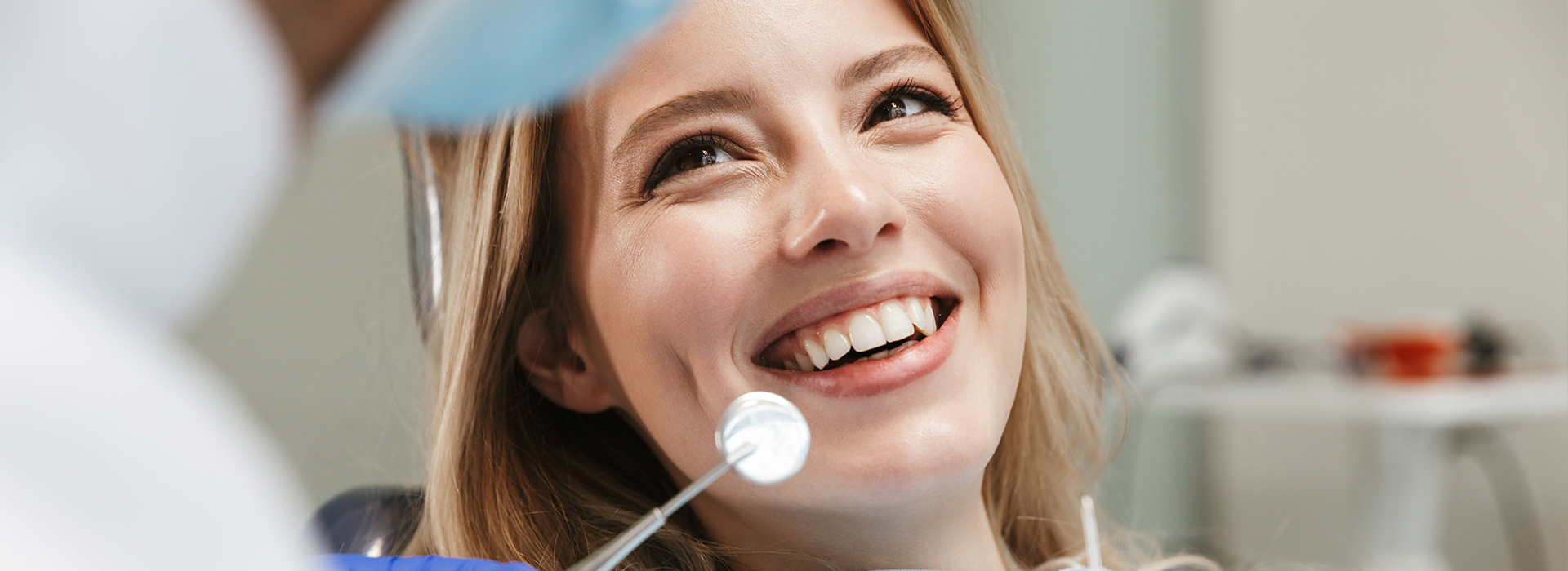A woman smiling at a camera, with a dental professional in the background.