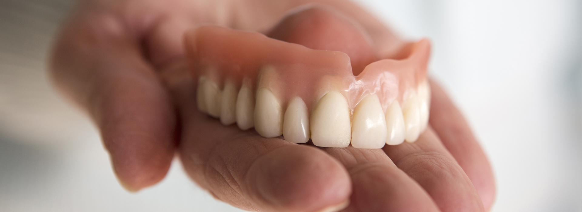 A person holding a set of artificial teeth in their hand.