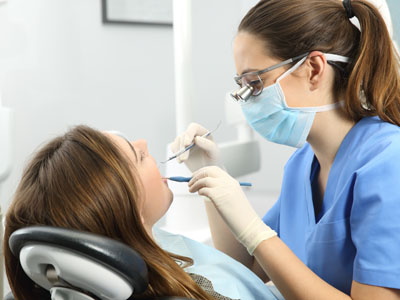 A dental hygienist in a white coat and mask is performing oral care on a patient, with the patient seated in a dental chair.